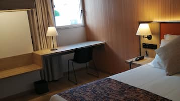 Una habitación de hotel con cama, escritorio, silla y dos lámparas de noche.