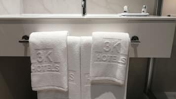 A bathroom with a white marble countertop, a modern faucet, and two towels hanging on a towel rack with "3K HOTELS" embossed on them.