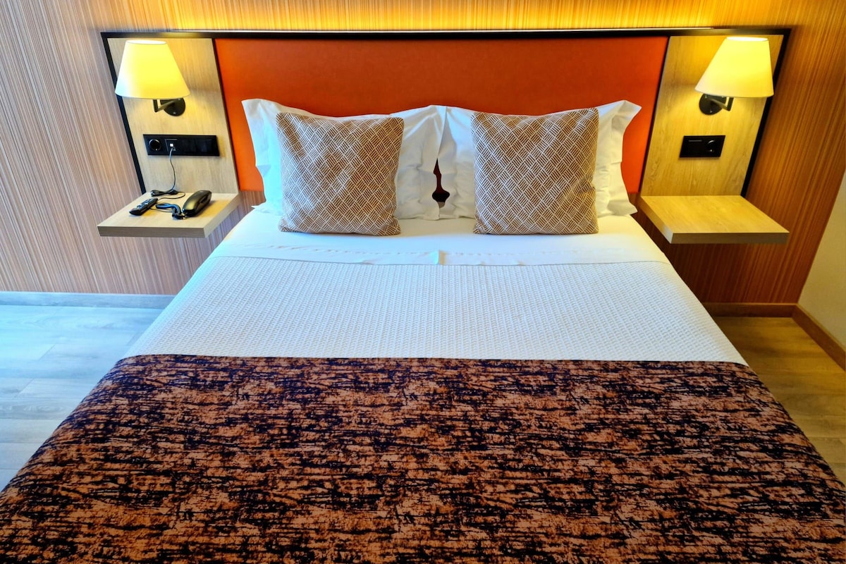 A neatly made bed with patterned pillows, two bedside lamps, and a wooden headboard.