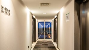 Corredor de hotel com placas de sinalização, um elevador e vista para o exterior à noite.