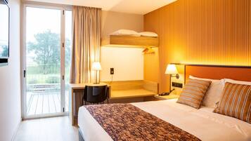 Habitación de hotel con cama, lámparas de noche, escritorio y vista al balcón exterior por una puerta corrediza.