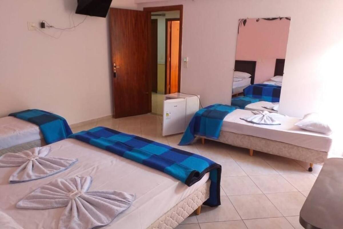 Une chambre d’hôtel avec trois lits, chacun recouvert d’une couverture à carreaux bleus et blancs, et des serviettes disposées en forme de nœud.
