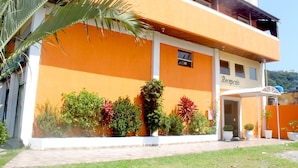 A two-story building with a reception area, surrounded by well-maintained greenery and a clear sky. - Hotel Sol do Pernambuco (Guarujá)
