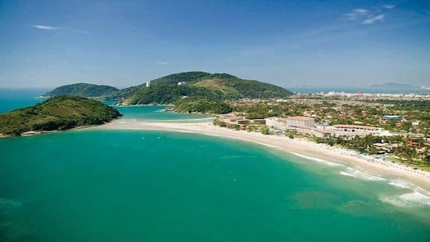 A coastal area with a beach, a hotel, and surrounding hills. - Hotel Sol do Pernambuco (Guarujá)
