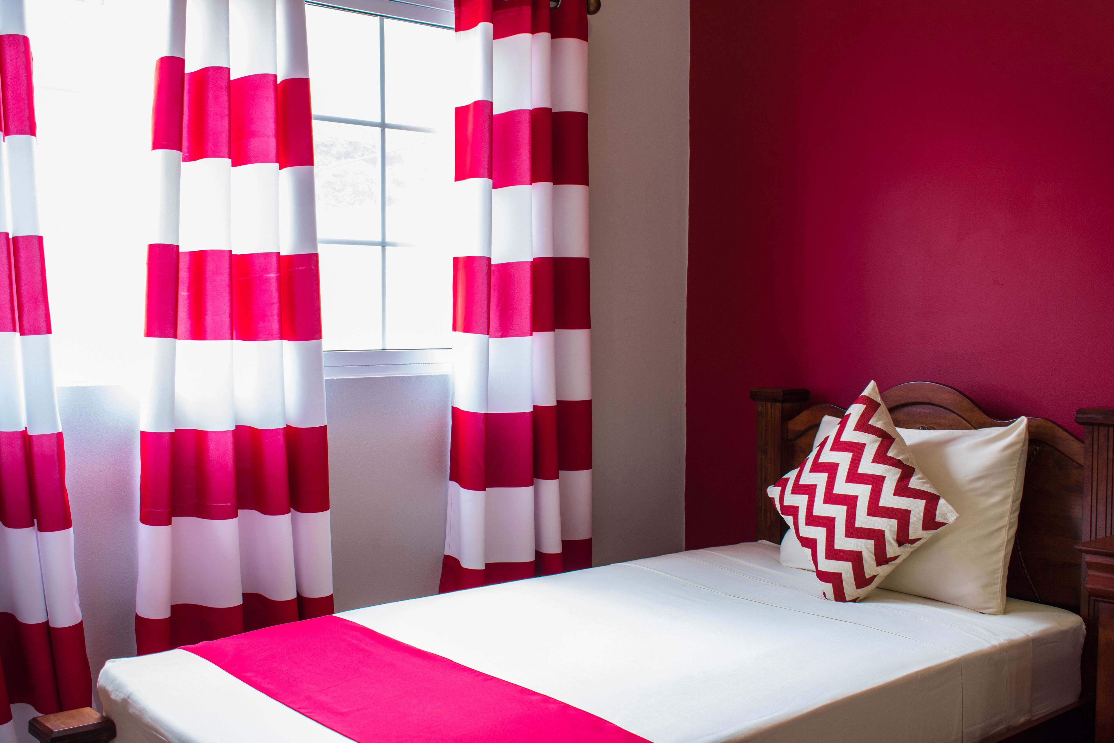 A bed with a white and red striped bedspread, a wooden headboard, and a pillow with a zigzag pattern.