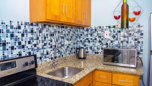 A kitchen with a granite countertop, stainless steel sink, wooden cabinets, a microwave, and a tiled backsplash. - Centrally located Oakland Guest Apartment I (Kingston)