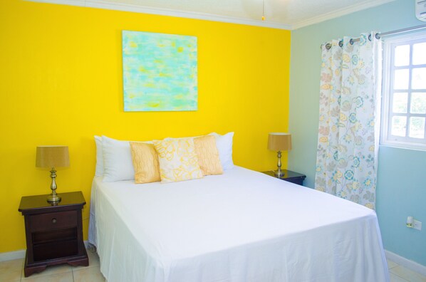 Un dormitorio con una cama, dos mesitas de noche, una ventana con cortinas y un cuadro en la pared.