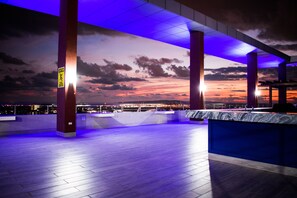 Ein Innenbereich mit Blick auf einen Sonnenuntergang, eine Bar mit einer Marmorplatte und ein Warnschild an einer Säule.