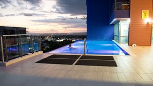 A rooftop pool area with a glass balustrade, a pool with blue lighting, and a city view at dusk. - 20 South Kingston Luxury Apartment (Kingston)