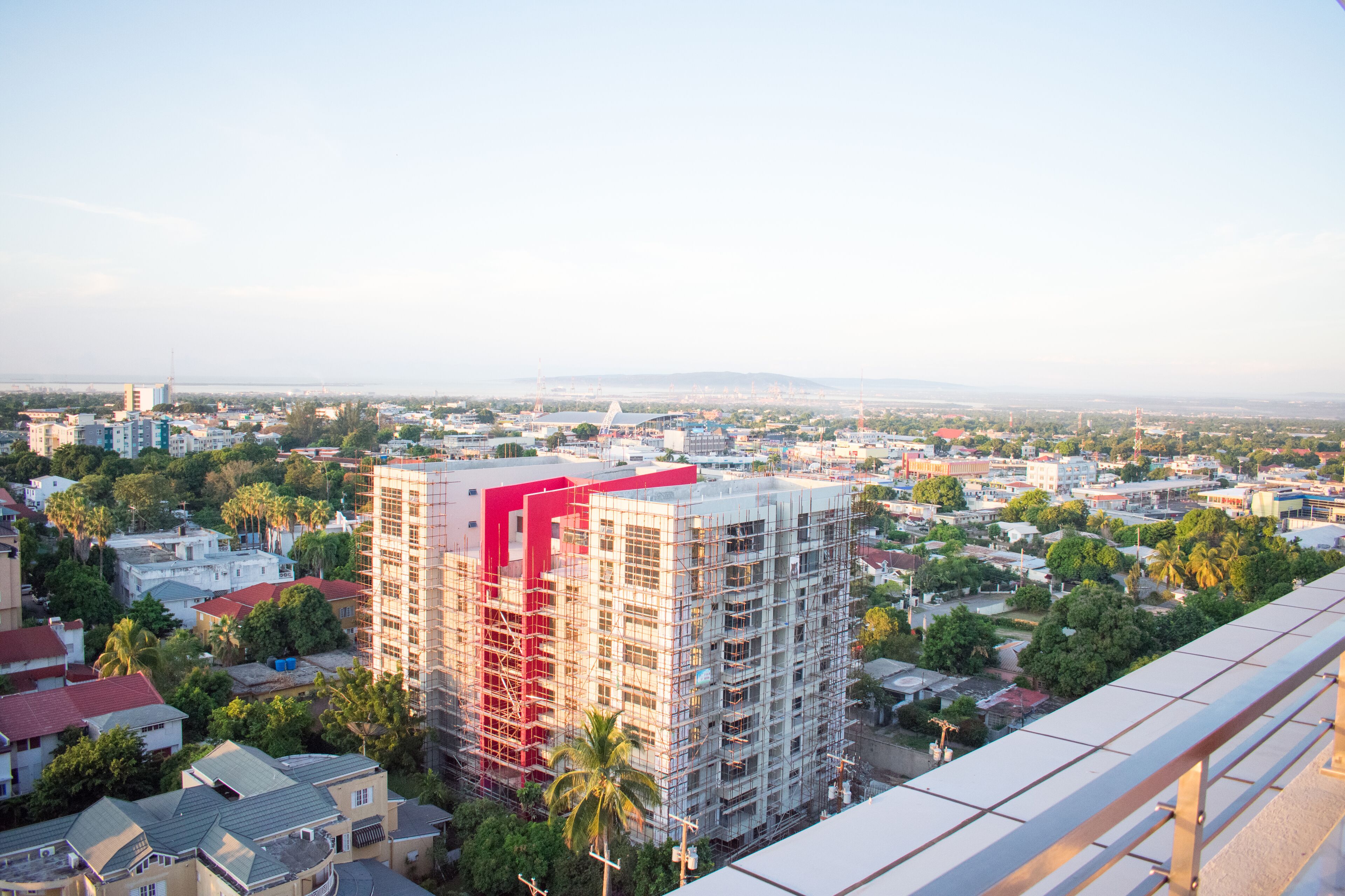 A high-rise building with a red facade, surrounded by residential buildings and greenery.