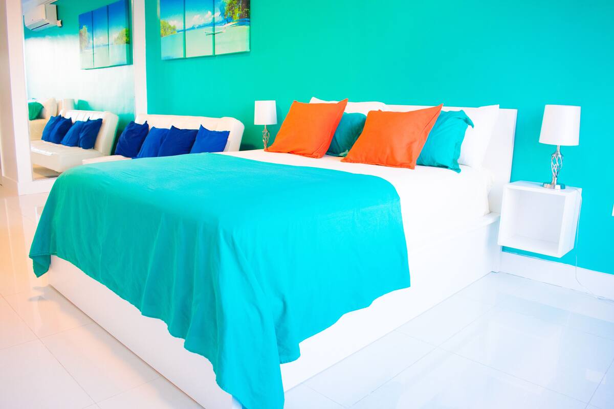 A bright room with a large bed, white furniture, and a teal wall.
