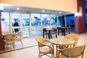 An indoor dining area with wicker chairs and tables, large windows, and a view of the street outside. - 20 South Kingston Luxury Apartment (Kingston)