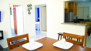A dining area with a wooden table and chairs, a kitchen in the background, and a door leading to another room. - Centrally located Oakland Guest Apartment II (Kingston)