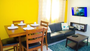 A living room with a dining table set for two, a sofa, a coffee table, and a TV mounted on the wall. - Centrally located Oakland Guest Apartment II (Kingston)