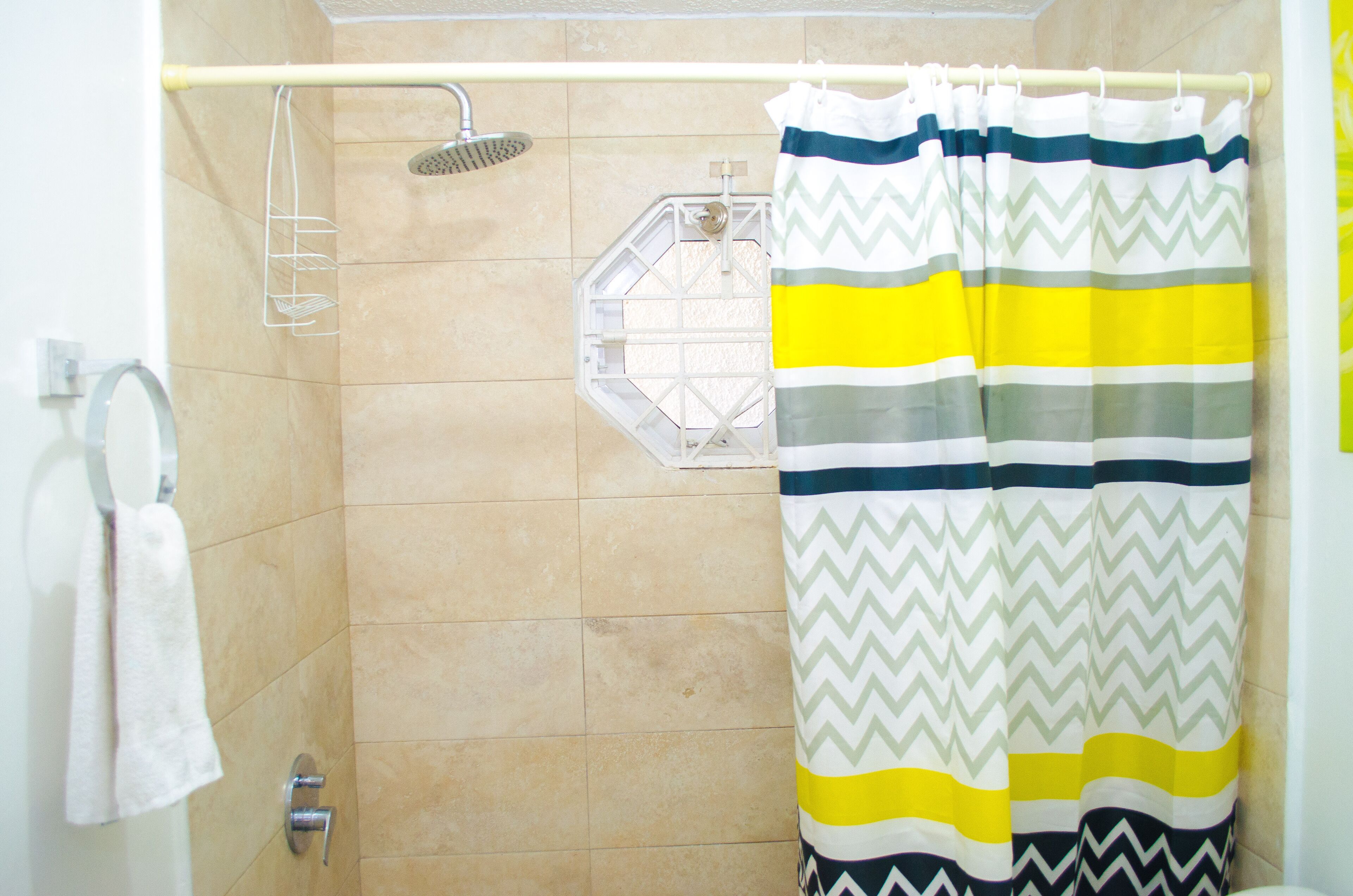 A shower area with beige tiles, a showerhead, a towel rack, and a striped shower curtain.