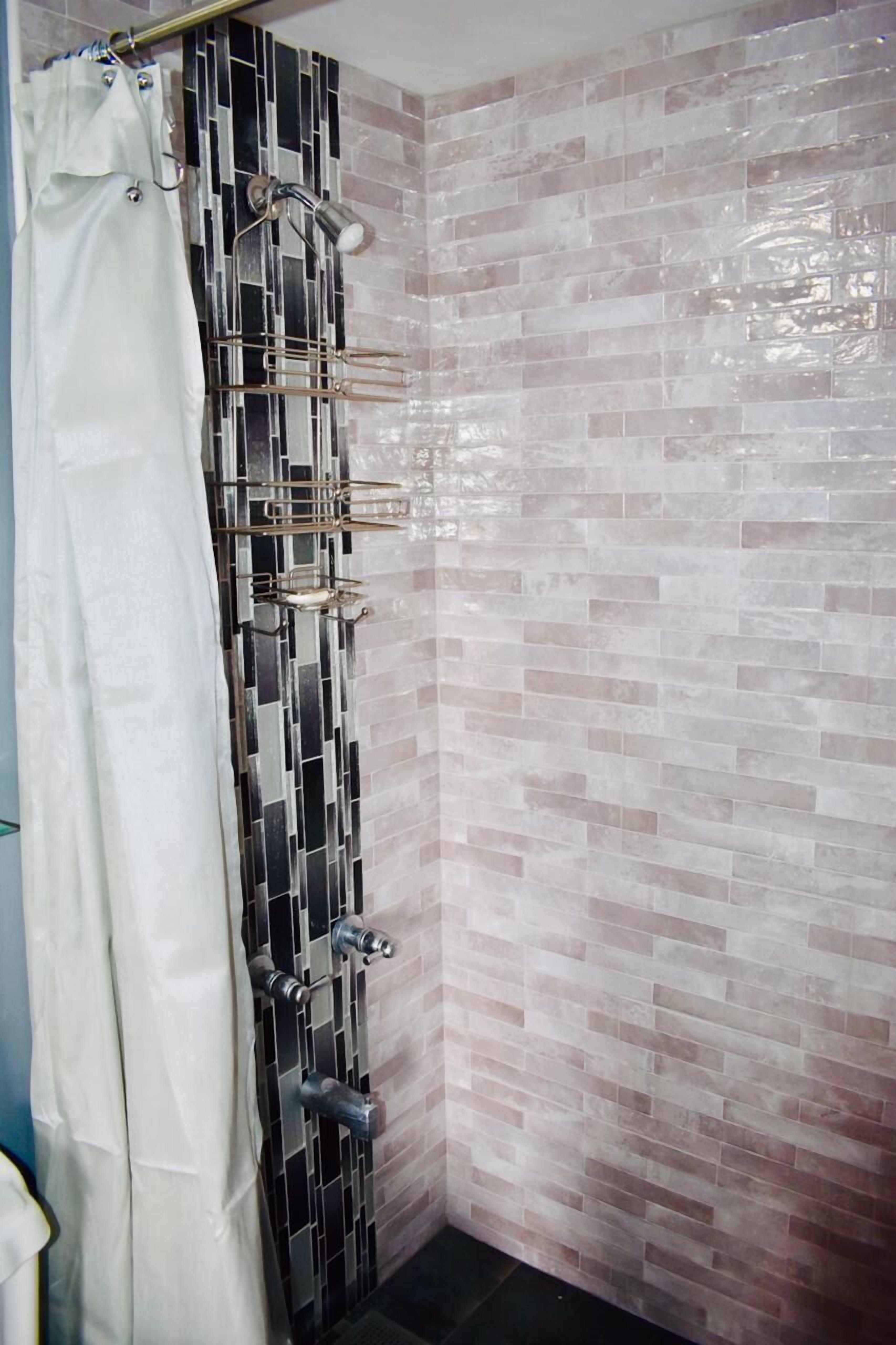 Ducha con pared de azulejos, cortina y cabezal metálico.