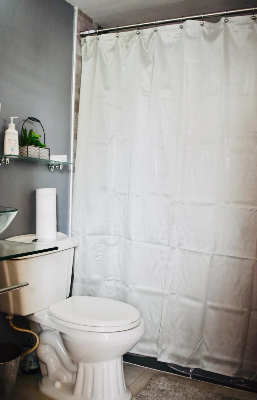 Une salle de bain avec des toilettes blanches, un lavabo en verre et un rideau de douche.