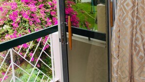 A balcony with a glass door, a white metal railing, and a view of a garden with pink flowers. - New Kingston Guest Apartment At Chelsea (Kingston)