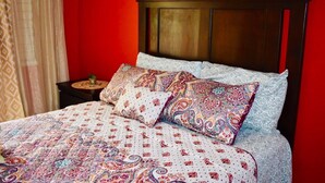 A bed with a patterned bedspread and pillows, a wooden headboard, and a nightstand with a decorative item. - New Kingston Guest Apartment At Chelsea (Kingston)