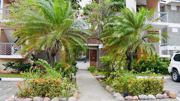 A residential building with a central entrance, surrounded by lush greenery and palm trees. - New Kingston Guest Apartment At Chelsea (Kingston)