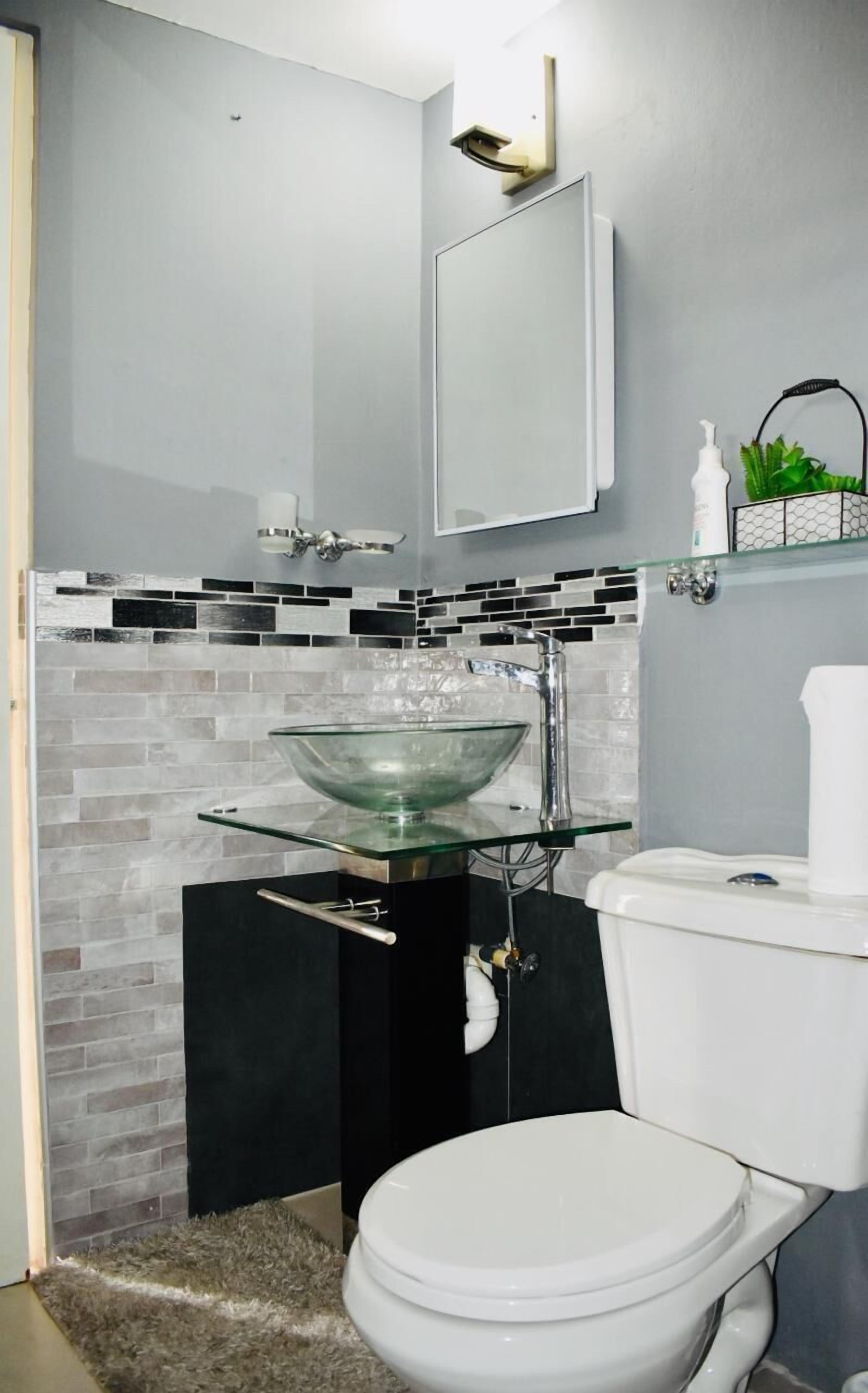 A modern bathroom with a glass bowl sink, a toilet, and a small shelf with toiletries.