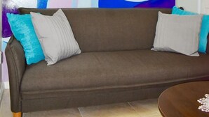 A living room with a large abstract painting on the wall, a brown sofa with teal cushions, and a wooden coffee table.