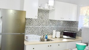 A compact kitchen with white cabinets, a stainless steel refrigerator, a microwave, and a sink.