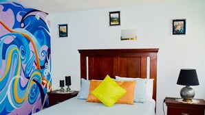 A bedroom with a bed, a nightstand, a lamp, and a wall with framed pictures.