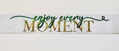 A sign with the text "enjoy every MOMENT" in glittery gold letters on a white background.