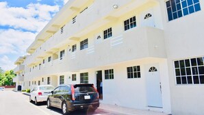 A multi-story building with a flat facade, large windows, and a parking area with cars.