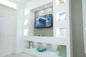 Een moderne woonkamer met een flatscreen-tv aan de muur, omringd door glazen schappen met decoratieve objecten.
