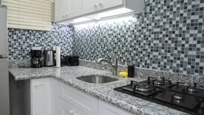 A kitchen with white cabinets, a granite countertop, a sink, a stove, and a tiled backsplash. - Kingston Guest Apartment At Valencia (Kingston)