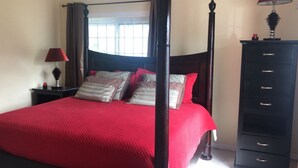 Un lit à baldaquin avec une literie rouge, une table de chevet avec une lampe et une commode avec des tiroirs.