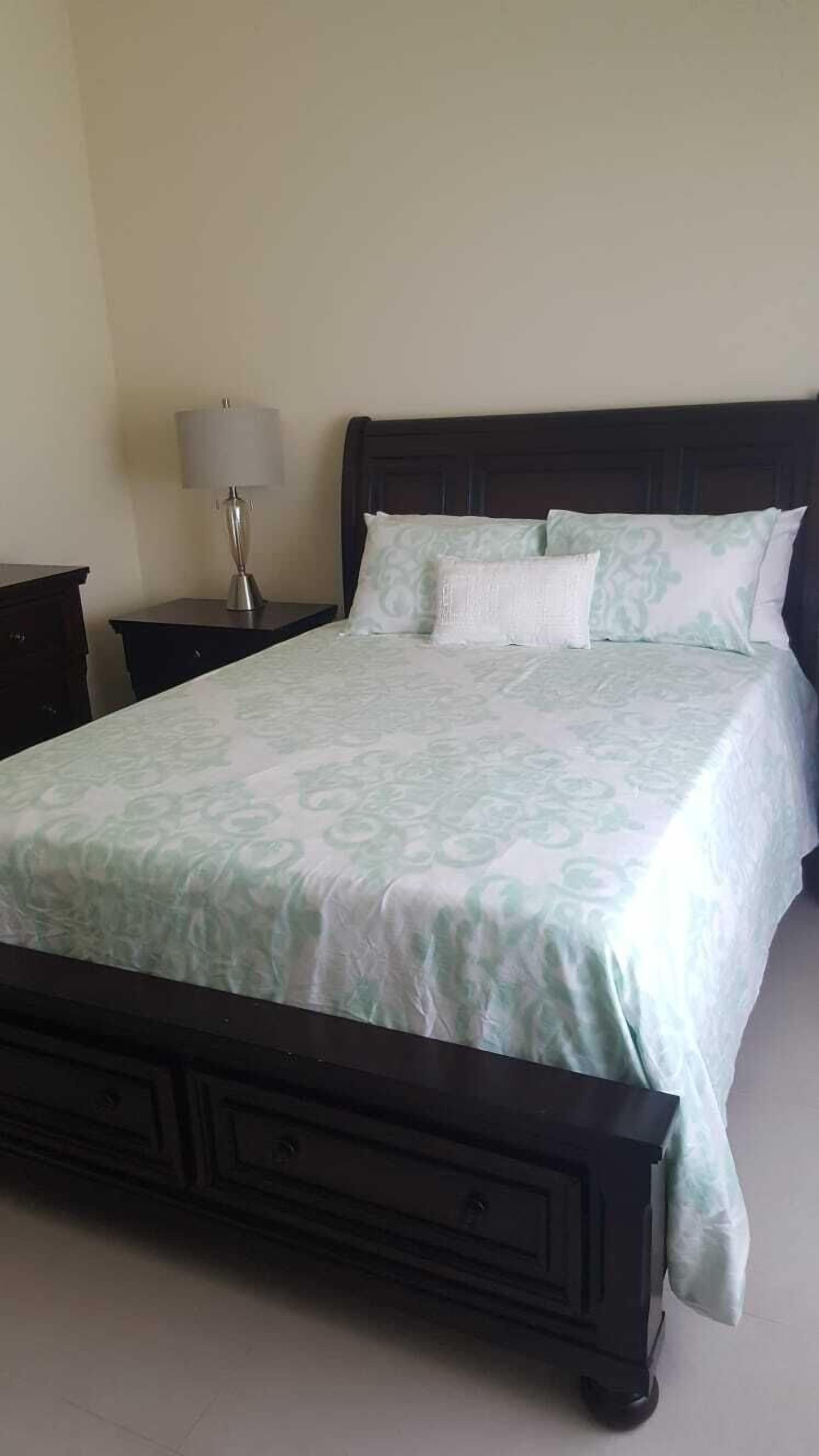 A neatly made bed with a patterned bedspread, a dark wooden headboard, and a bedside table with a lamp.