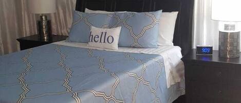 A neatly arranged bedroom with a bed, bedside tables, a nightstand, a lamp, a clock, and an air conditioning unit.