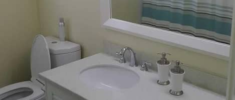 Un baño con lavamanos blanco, espejo, inodoro y cortina de ducha.