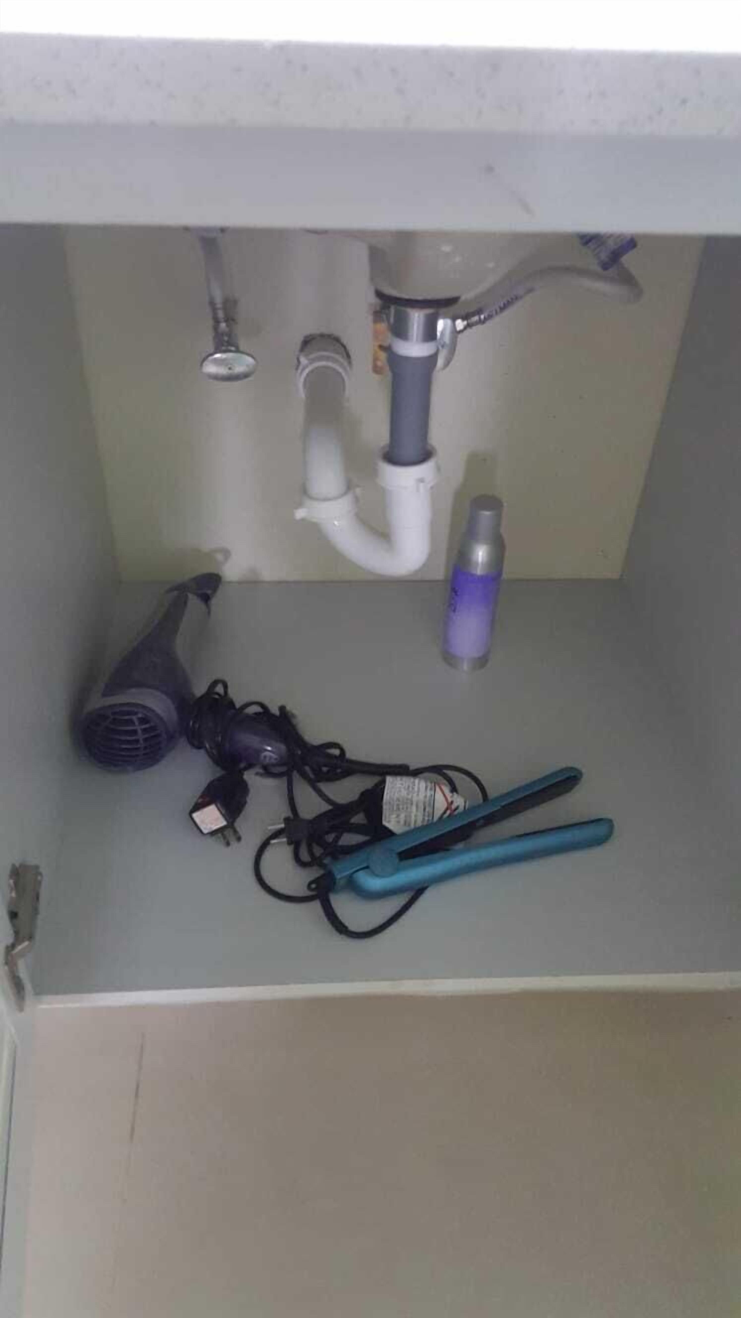 A bathroom sink with a hairdryer, a bottle of hand sanitizer, and a pair of scissors.