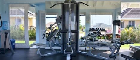 A gym with various exercise machines, a bench, and dumbbells.