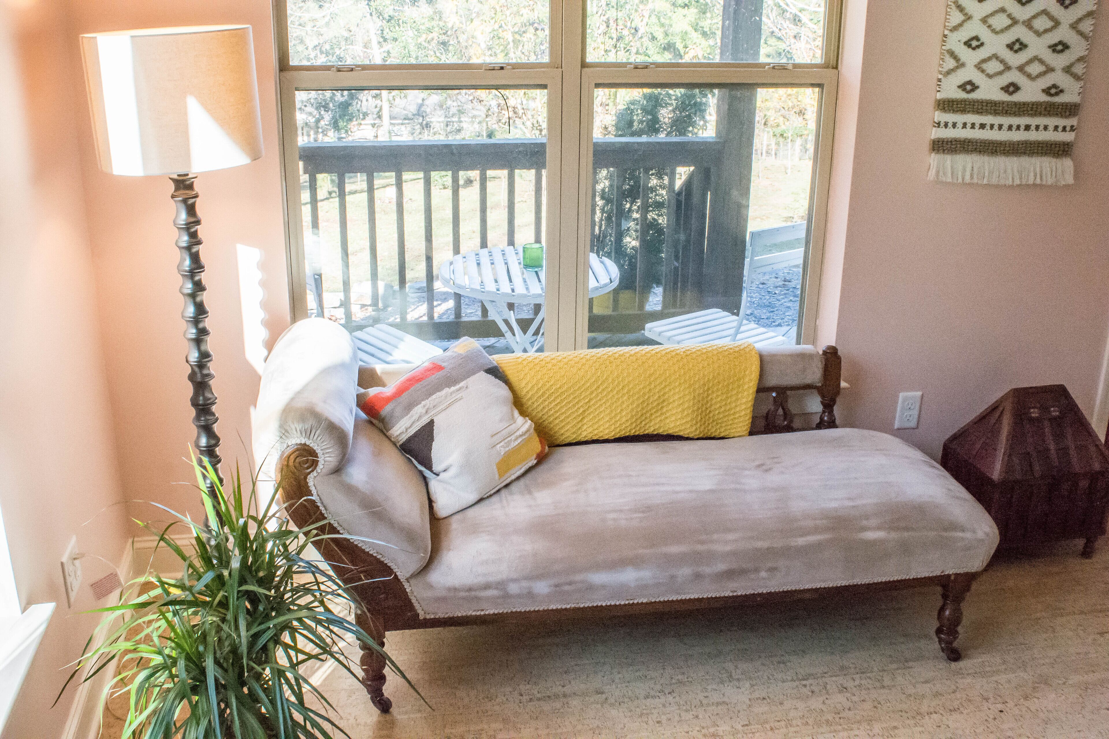 A cozy room with a cushioned bench, a floor lamp, and a view of an outdoor deck with chairs.
