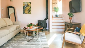 Ein Wohnzimmer mit einer Couch, einem Couchtisch mit Pflanzen, einem Kamin, einer Treppe und einem an der Wand befestigten Fernseher.