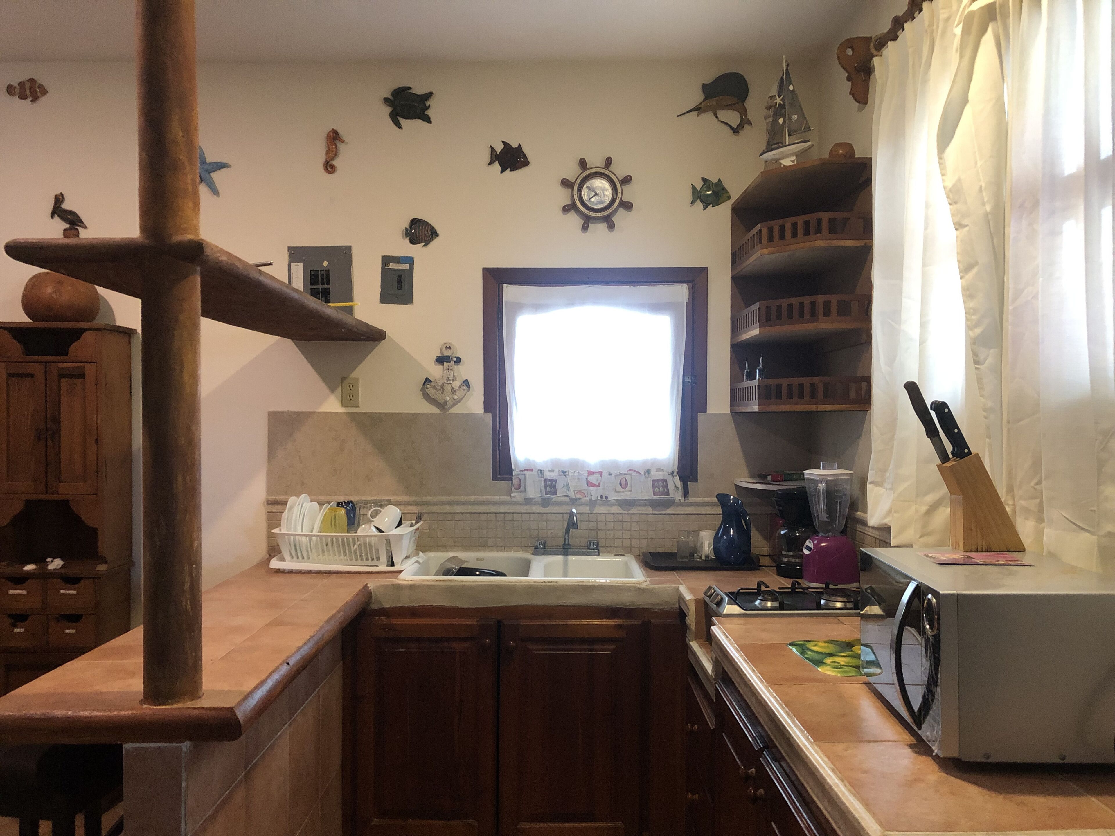 Una cocina con armarios de madera, un lavamanos, una estufa y varios electrodomésticos. Se observan peces decorativos y un barco en la pared.