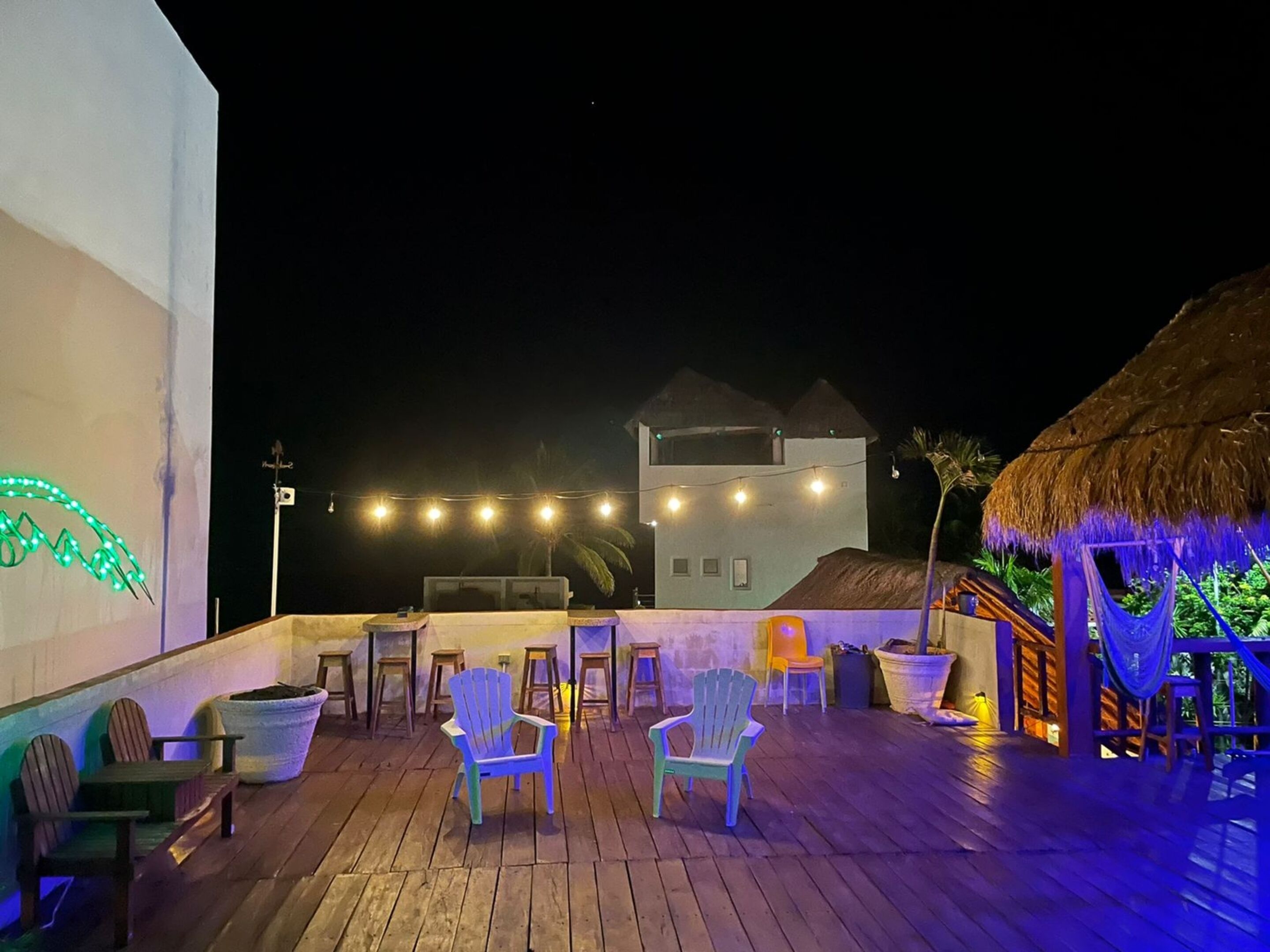 Eine Holzterrasse mit Stühlen und Tischen, ein Gebäude mit einem Strohdach und Lichterketten.