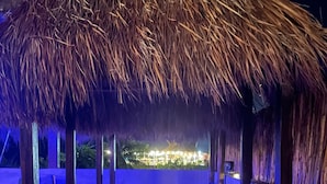 A thatched-roof outdoor seating area with a view of a resort.