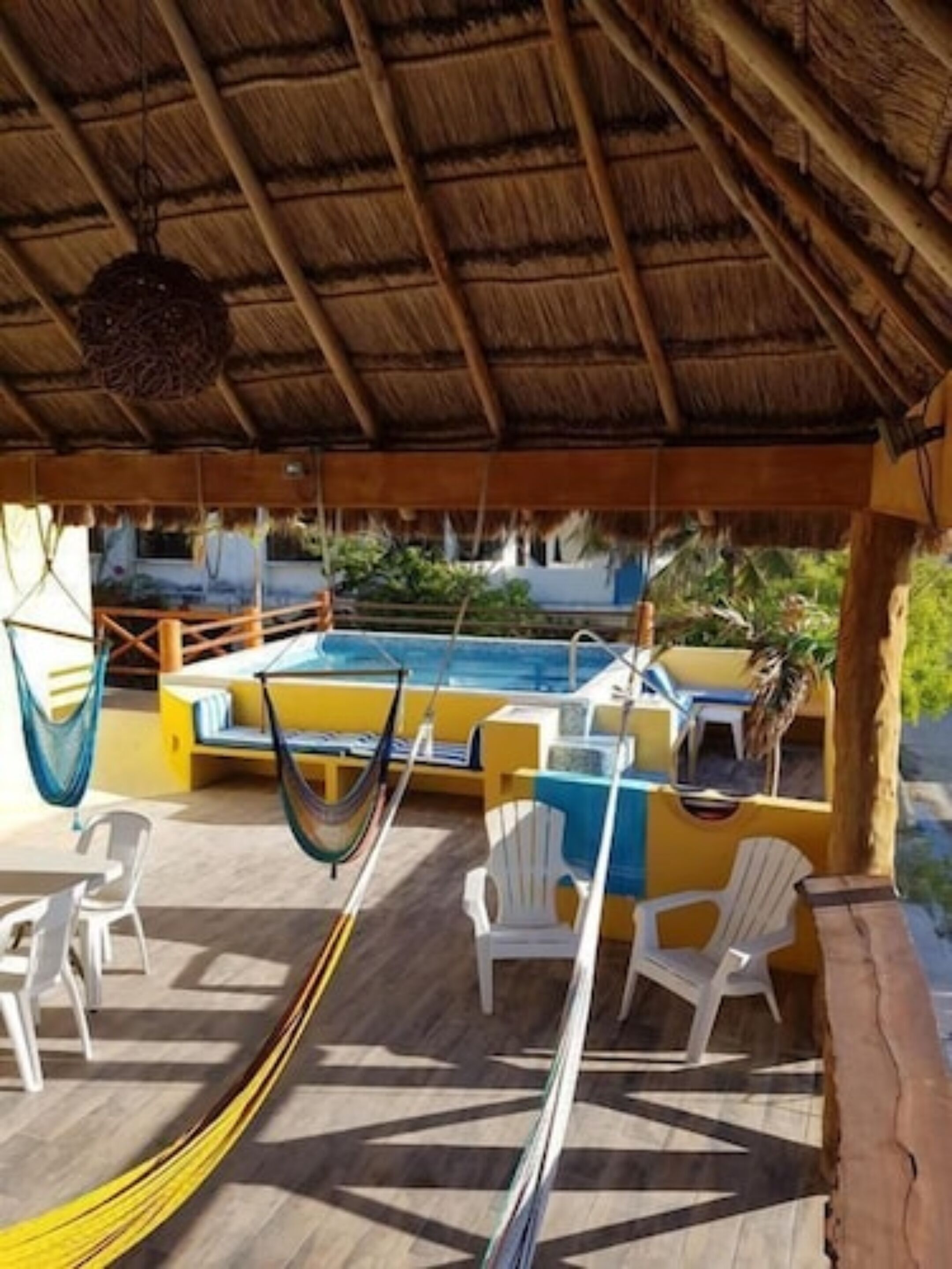 A covered outdoor area with a pool, white plastic chairs, and a hammock.