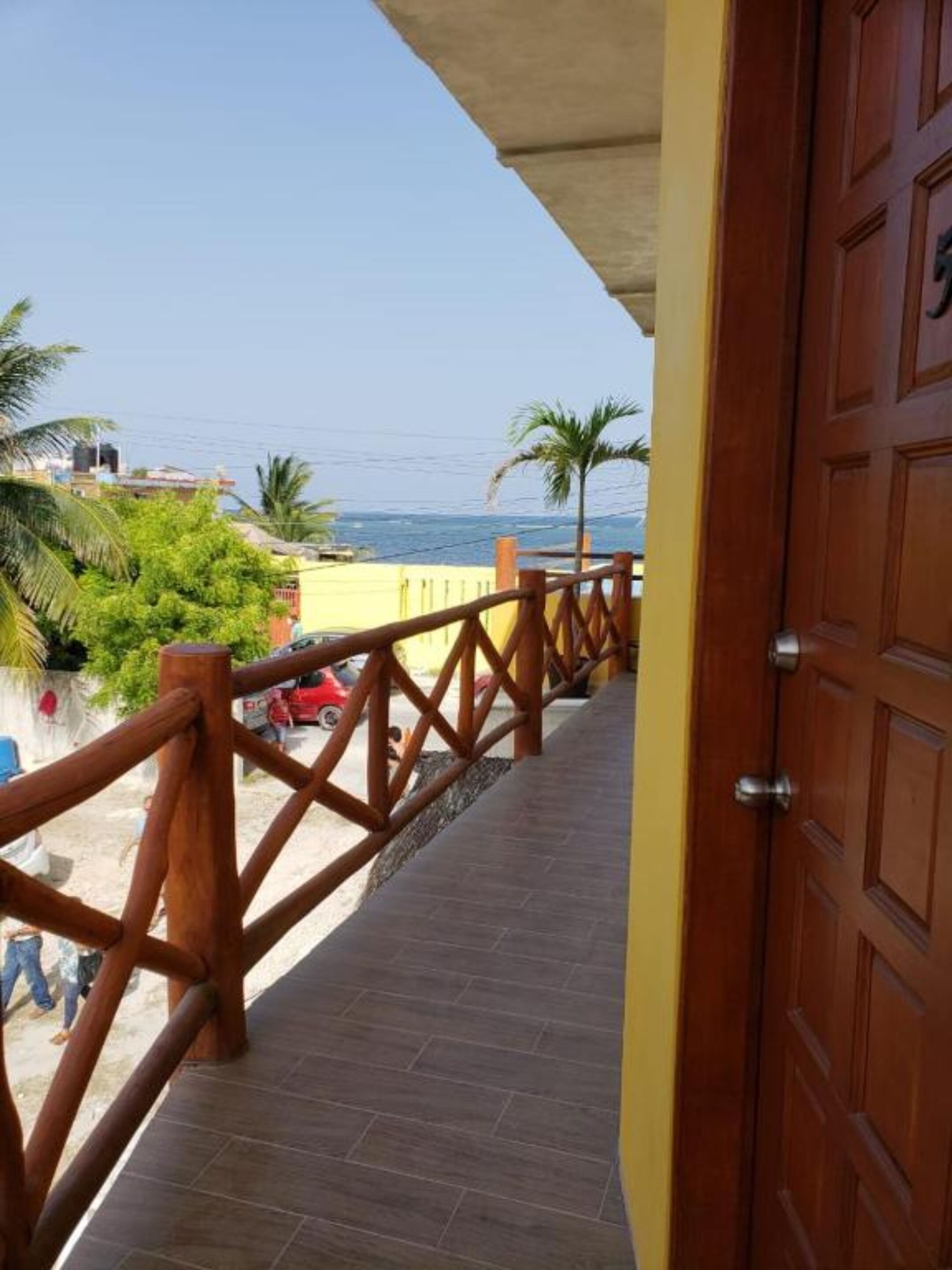 A wooden balcony with a view of the sea and palm trees.