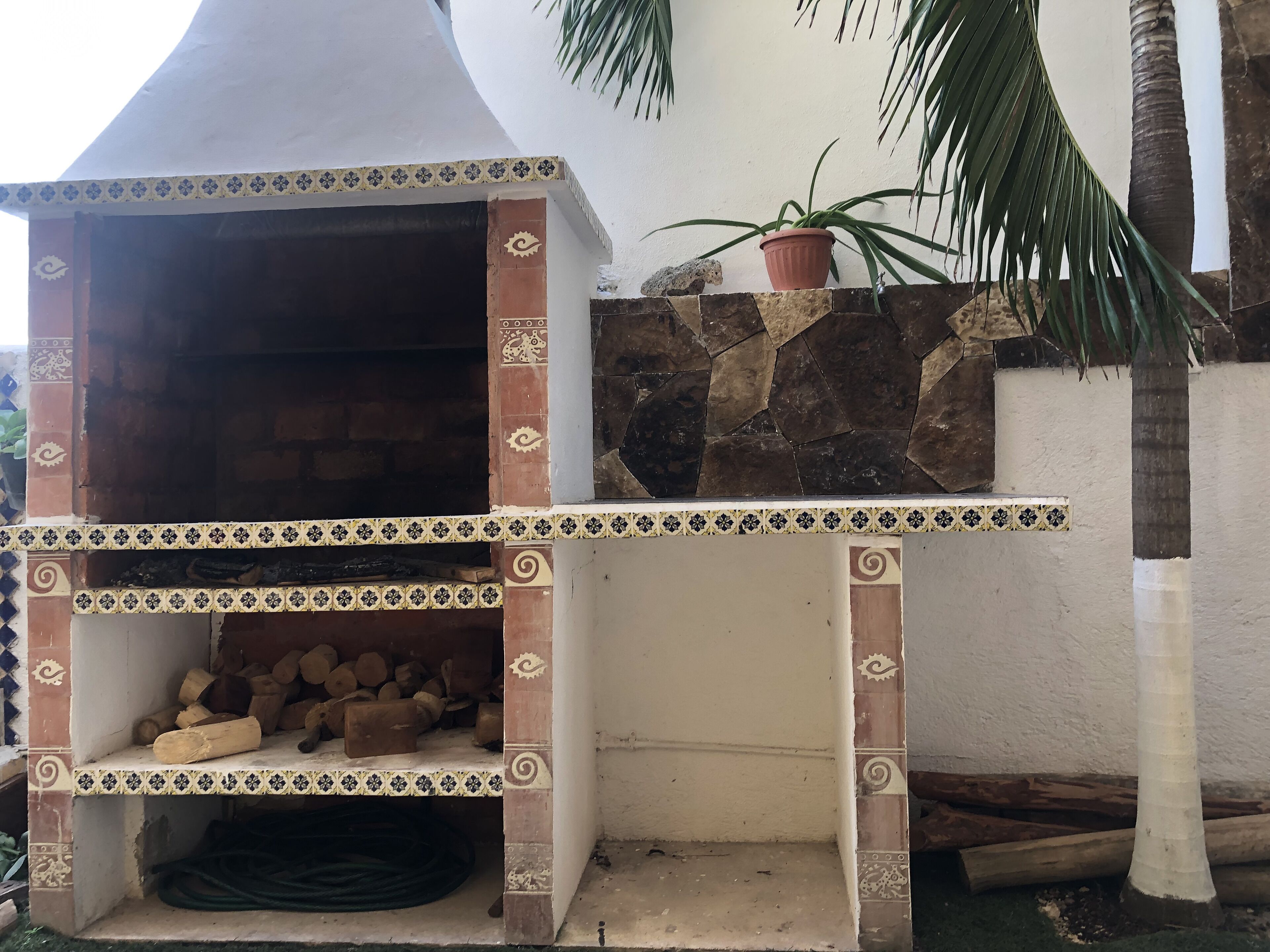 A brick-built outdoor oven with decorative tiles, a stone wall, and a potted plant.