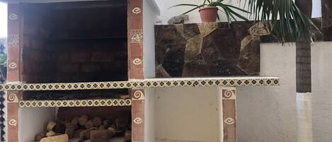 A brick-built outdoor oven with decorative tiles, a stone wall, and a potted plant.
