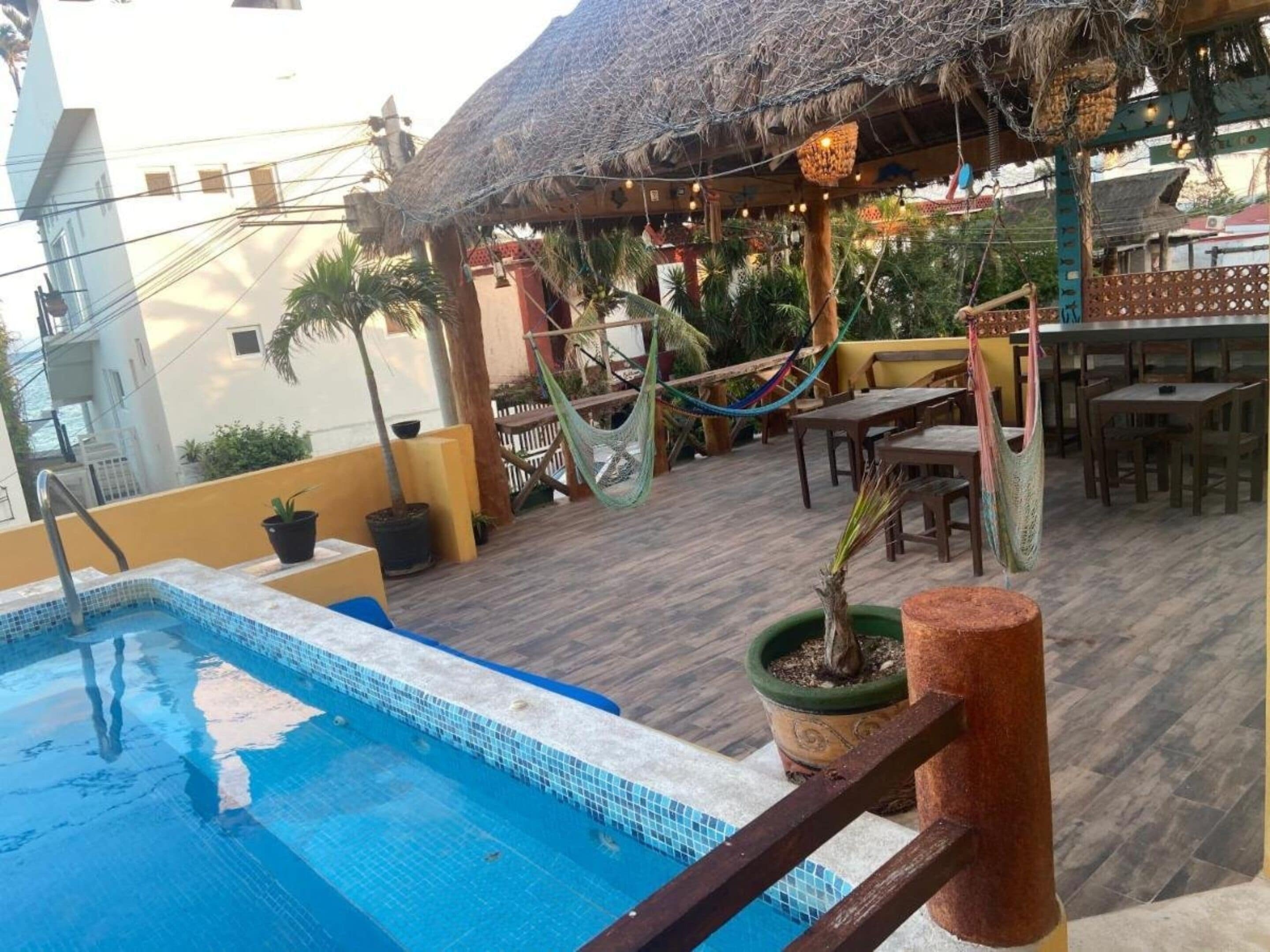 A pool area with a thatched roof structure, outdoor seating, and potted plants.