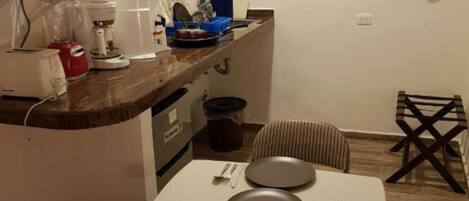 Une cuisine compacte équipée d’un four à micro-ondes, d’une machine à café et d’un petit coin repas avec une table et des chaises.