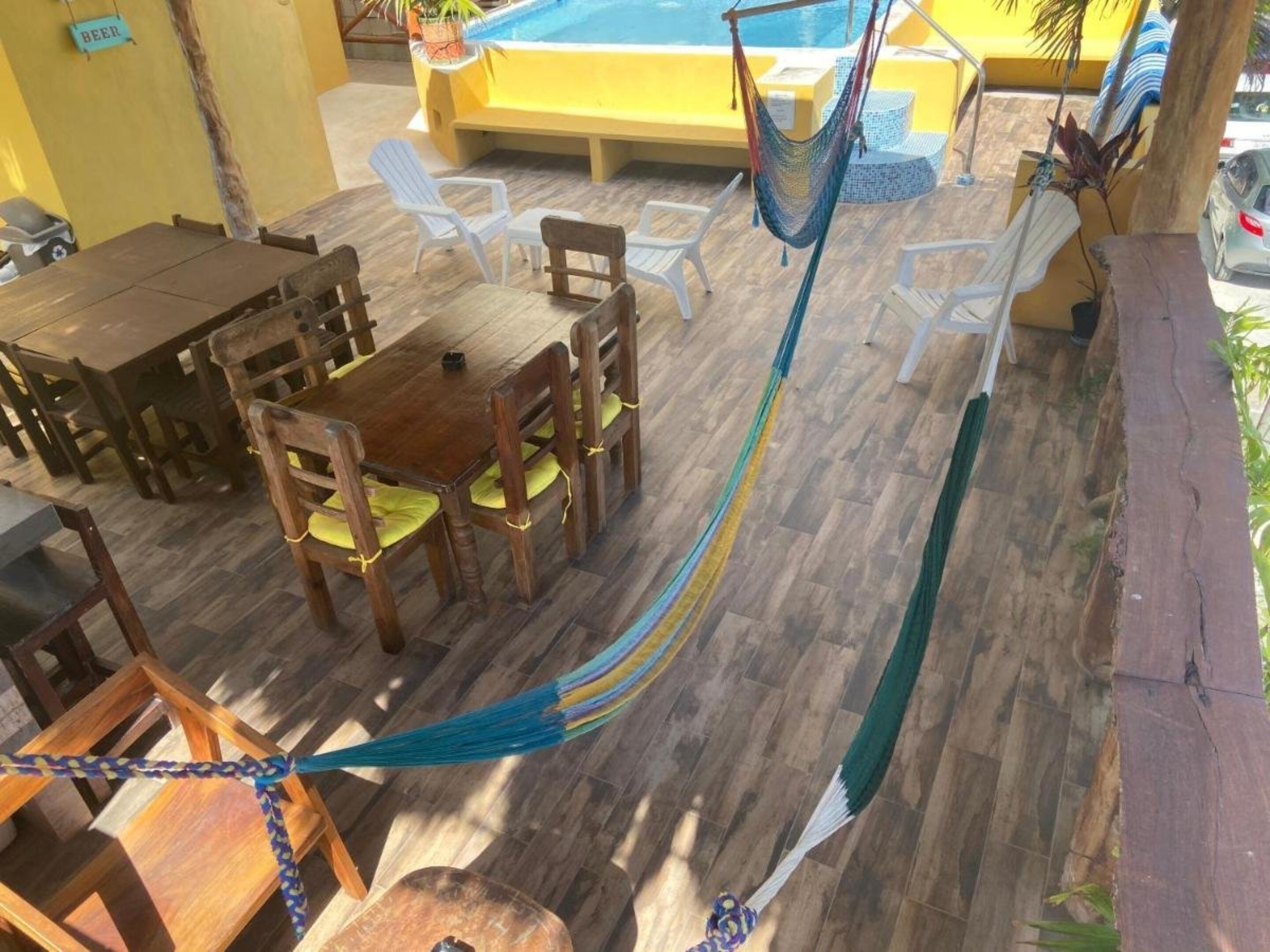 Un espace aménagé au bord de la piscine, avec des meubles en bois, un hamac et un panneau indiquant la zone où l’on peut consommer de la bière.